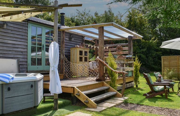 A wooden deck with a hot tub and a white bathrobe hanging outside a cabin at Burr 2 Shepherds Hut in Swimbridge near Barnstaple