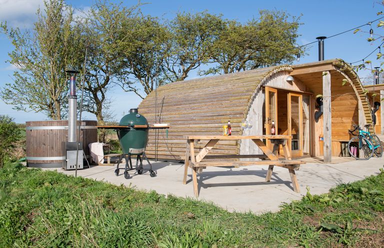 An outdoor area with a wooden glamping pod wooden picnic table barbecue grill and hot tub at Glamping Pod 1 Comfort in Lebberston