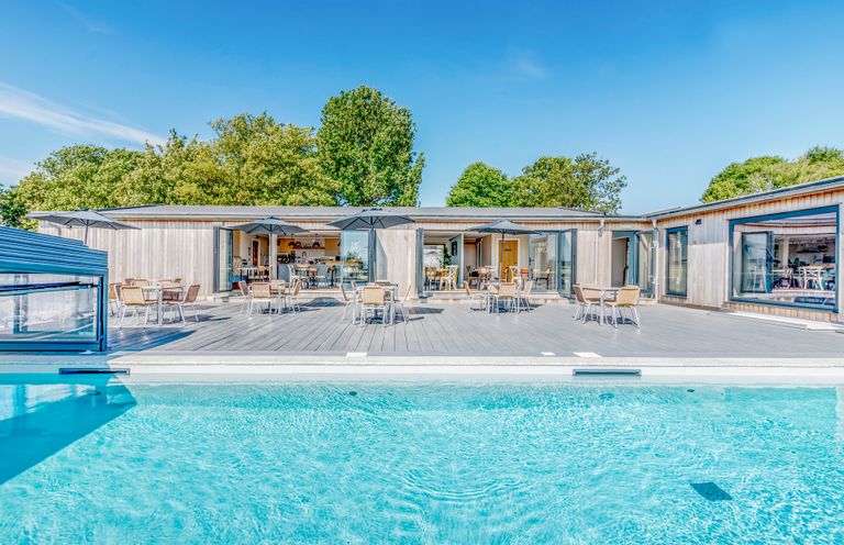 An outdoor area with a swimming pool and tables at Chalet 2 at Landscove Holiday Park Brixham