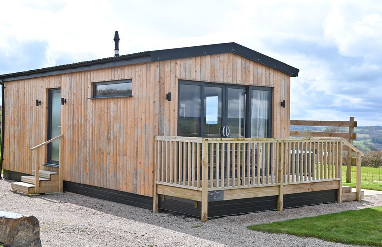 A wooden cabin with a small deck and glass double doors at Cae Dafadd in New Mills near Llanfair Caereinion