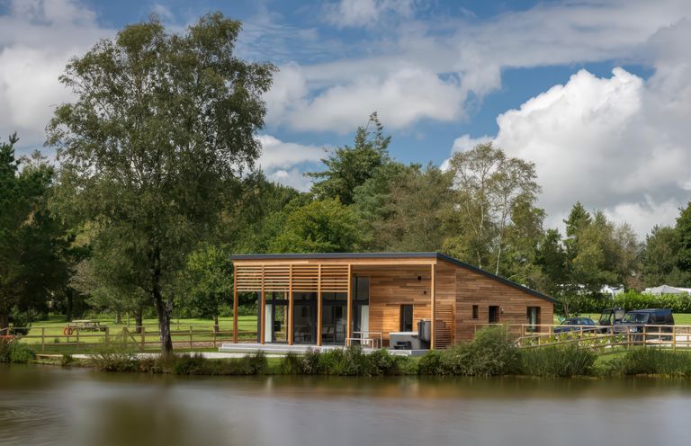 A wooden house near a lake with trees and cars at Silver Birch in Dolton