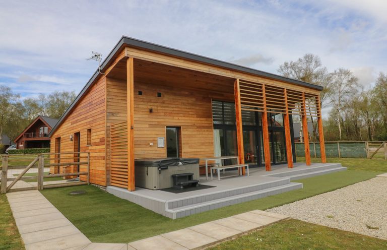 A wooden house with a covered patio with a hot tub and outdoor table and bench at Cherry in Dolton