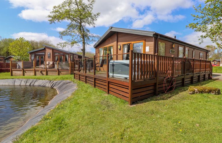 Two wooden lodges with fenced decks near a small pond at Coniston in Carnforth