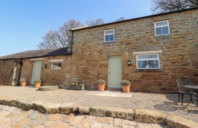 An outdoor view of a stone building with a green door at Cragg Lodge West Woodburn