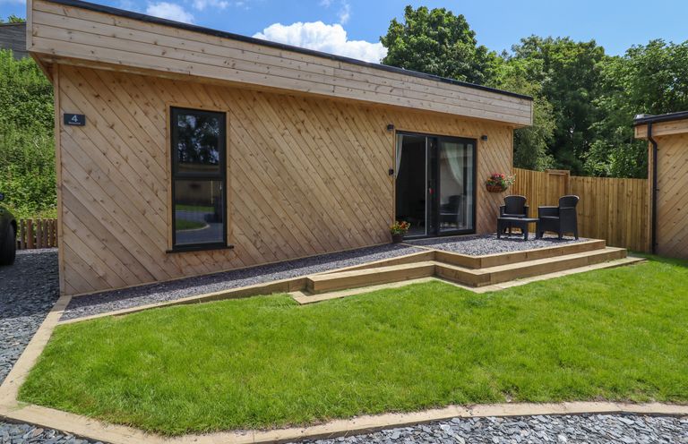 An outdoor patio area with two black chairs and a table beside a wooden lodge with sliding glass doors at Valley Lodge 4 - North Wales Eco Lodges in Graigfechan near Ruthin