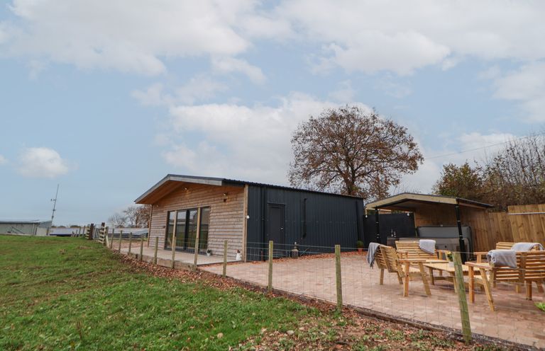 An outdoor patio area with wooden chairs and tables next to a small wood and metal building at Elliw in Bontuchel near Ruthin