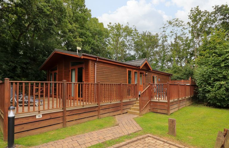 A wooden cabin with a surrounding deck and outdoor seating in a wooded area at Templar Rise 16 - Devon Comfort Finlakes Holiday Park near Chudleigh