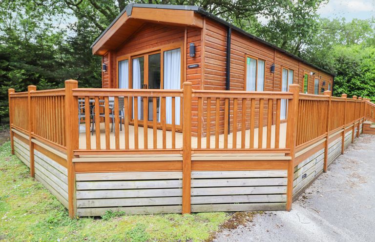 A wooden cabin with a fenced deck surrounded by trees at Tawny Owl Lodge in Coniston 4 White Cross Bay near Windermere