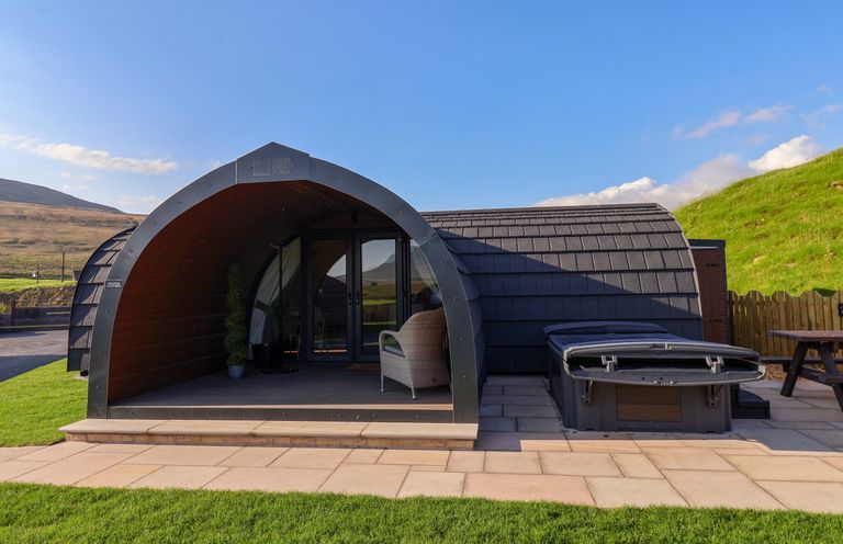 An arched cabin with a chair and potted plants next to a hot tub and picnic table at Oyster Catcher in Chapel Le Dale near Ingleton