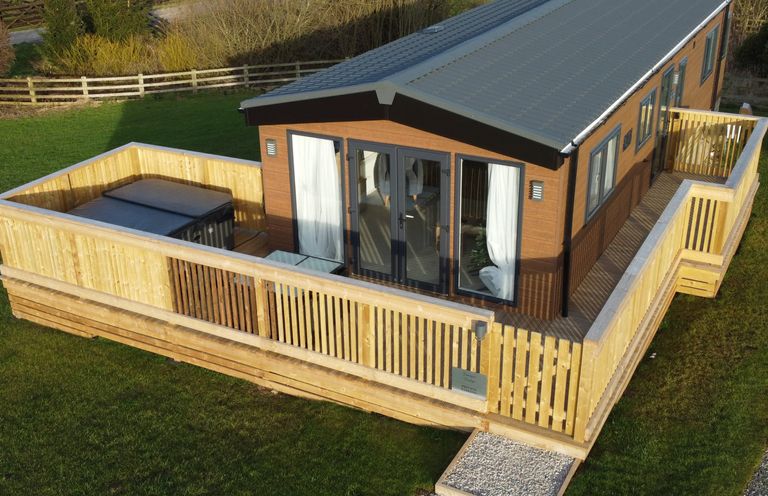 A single-story wooden lodge with a fenced wooden deck and a hot tub on the deck at Juniper Lodge in Whitby