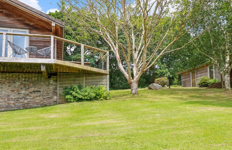 A grassy garden with trees and wooden houses with a deck and two chairs at 3 Lake View in Lanreath