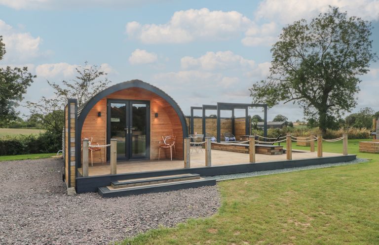 A wooden pod structure with a deck and outdoor seating in a grassy area at Paradise in Kenstone near Hodnet