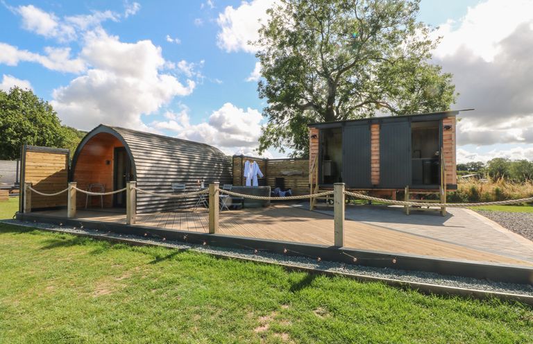 A wooden pod and a small wooden building with doors on a deck with rope fencing at Hawkstone Kenstone near Hodnet