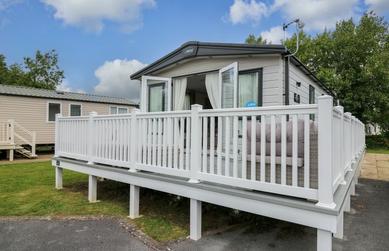 A raised mobile home with white railings and outdoor seating at Osprey 6 in Kiln Park Tenby