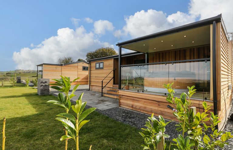 A wooden lodge with glass balcony and green plants in a grassy yard at Enia Lodge 2 Llanelidan near Corwen