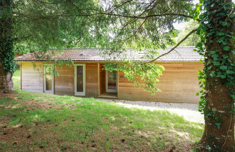 A wooden house with three glass doors surrounded by trees and grass at 10 Waters Edge in Lanreath