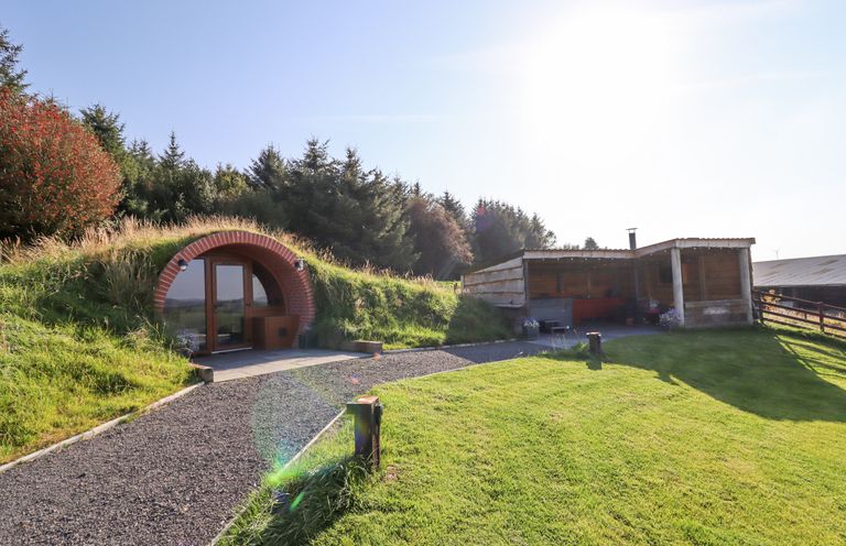 A hobbit style earth house entrance and wooden shelter in a grassy yard at Cae Bach in Cyffylliog near Ruthin