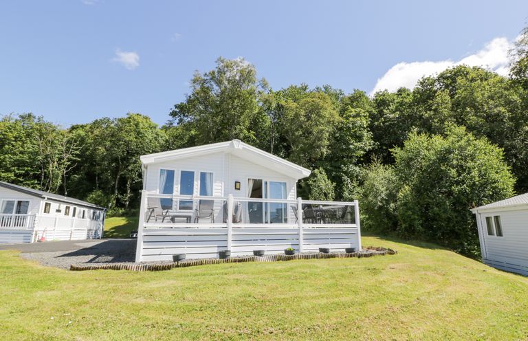 A white cabin with a deck and outdoor furniture surrounded by grass and trees at Bethany's Retreat in Wemyss Bay
