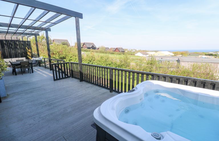 An outdoor deck with a hot tub table and chairs with houses and greenery in the background at Bay View in Portreath