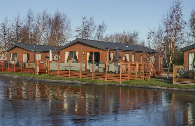Wooden lodges with outdoor seating beside a frozen pond at The Three Bears Lodge Coniston Drive 11 South Lakeland Leisure Village near Warton