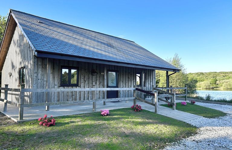 A wooden lodge with a deck and flowers outside at Kingfisher Lodge in Treverbyn near St Austell
