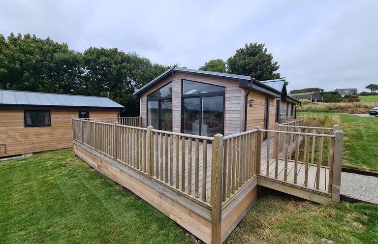 A wooden house with large windows and a fenced wooden deck surrounded by grass at Cove Lodge in Ilfracombe