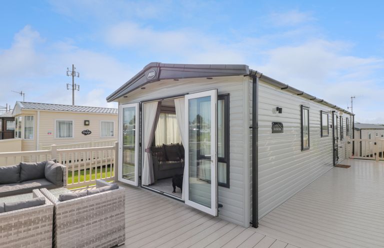 An exterior view of a mobile home with open patio doors a seating area on the deck at Drake 11 in Cayton Bay