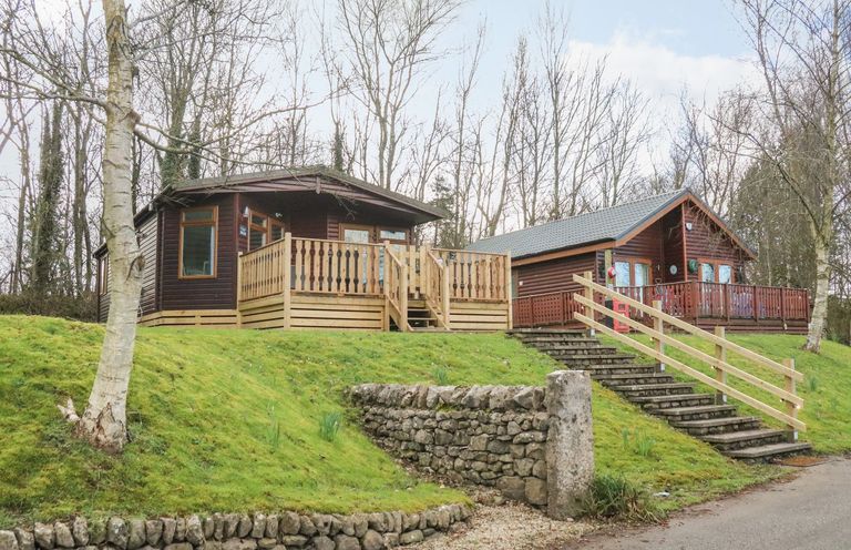 Two wooden lodges on a grassy slope with stone retaining walls and stairs at Park View Lodge Arnside 7 South Lakeland Leisure Village near Carnforth