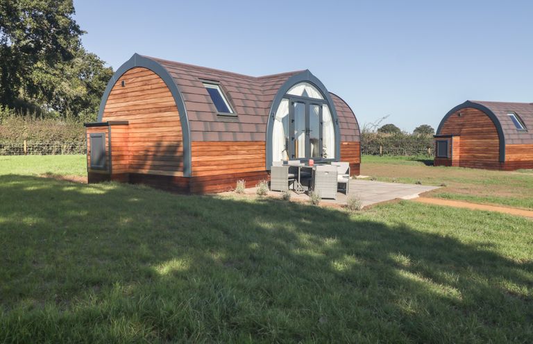 Two wooden arched cabins with patio furniture outside on grassy land at Leadon View Oak in Upleadon near Newent