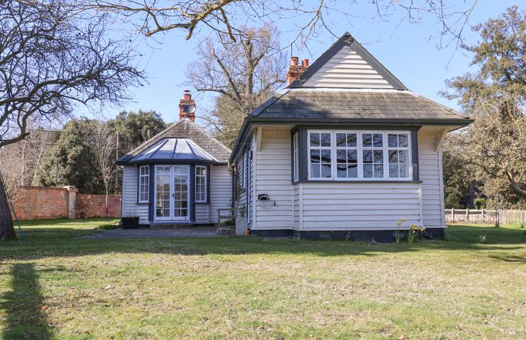 A house with white wooden siding and multiple windows surrounded by trees and grass at Holm Oak Lodge in Tendring near Weeley