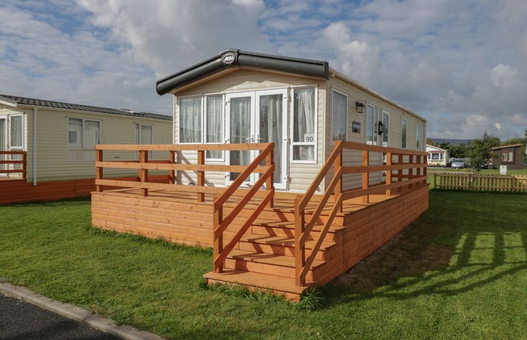 A mobile home with a wooden deck and steps on a grassy lawn at Elm in Denny