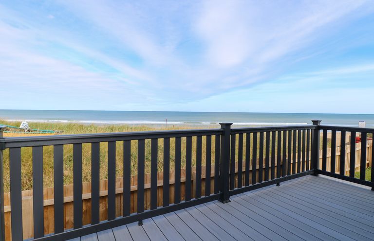 A deck with black railing overlooking grassy dunes and a beach at Seaview Lodge in Bacton