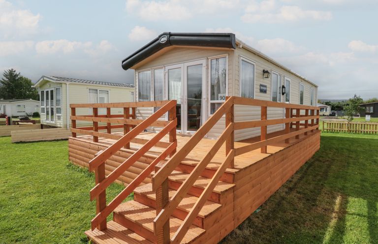 A mobile home with a wooden deck and stairs on a grassy area at Hazel in Denny
