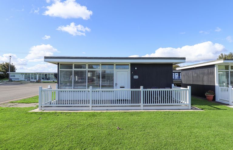 A single-story black and white house with a small front porch and green grass at 104 The Laurels in Chapel St Leonards