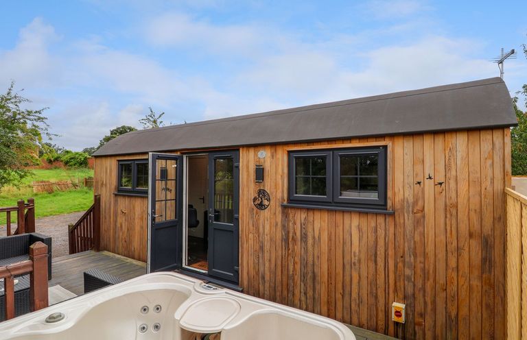 Exterior view of a wooden cabin with black framed windows and open double doors next to a hot tub at The Retreat in Bangor-On-Dee