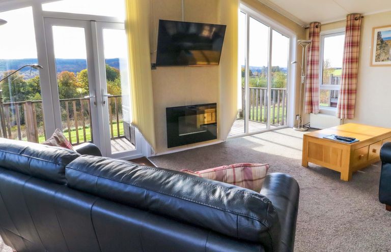 A living room with leather sofas a wooden coffee table a wall-mounted tv and large windows at Crathie Lodge in Banavie near Caol