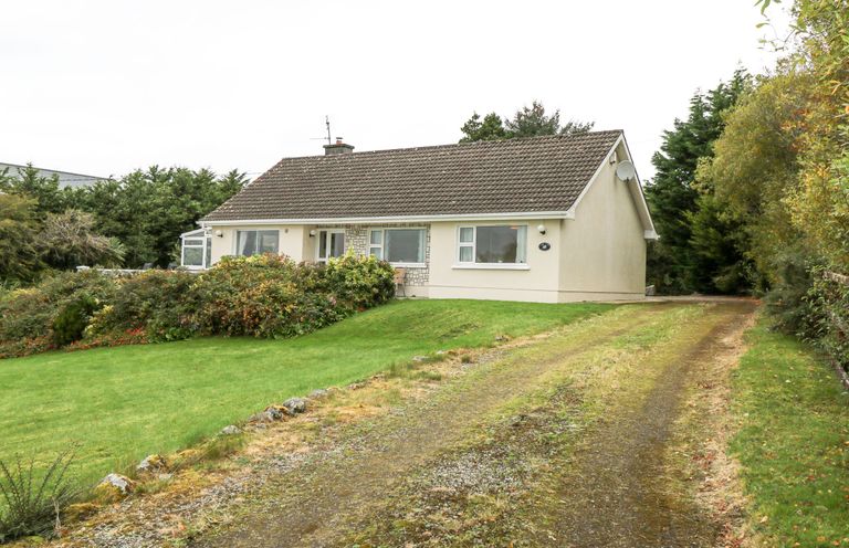 A single story house with a tiled roof surrounded by grass and shrubs at Lakeview Lodge in Knockmore County Mayo