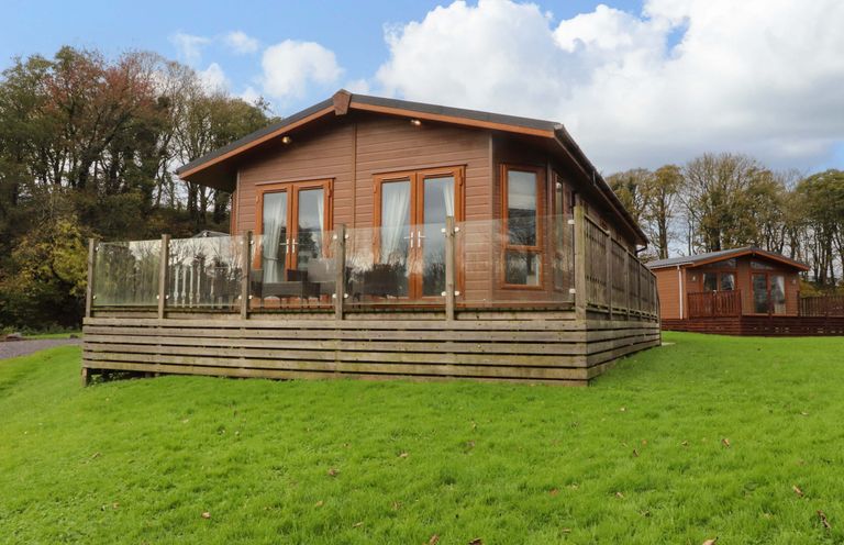 A wooden lodge with glass railing on a grassy hill with trees in the background at Lakeview Lodge in Forton near Garstang
