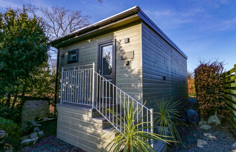 An exterior view of a small wooden cabin with stairs and metal railing at Elderflower Lodge in Allithwaite near Cartmel