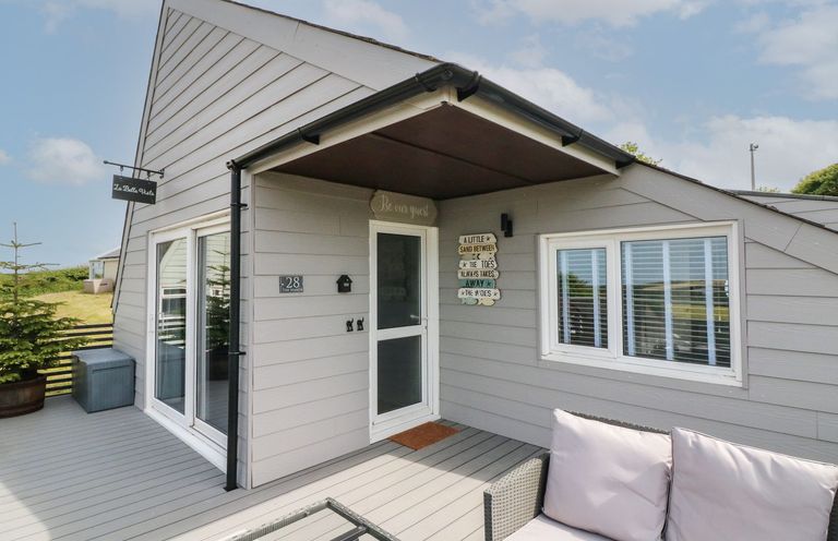 The exterior entrance of a gray wooden house with a sliding glass door a small sofa and table on the deck at La Bella Vista in Kilkhampton