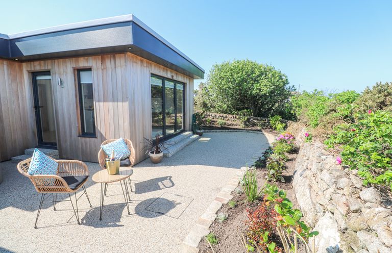 A garden patio with two chairs and a small table outside a wooden house at Little Victory in Pendeen