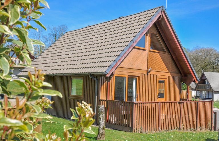 A wooden house with a sloped roof and a deck at Cornish Woodland Retreat near St Tudy