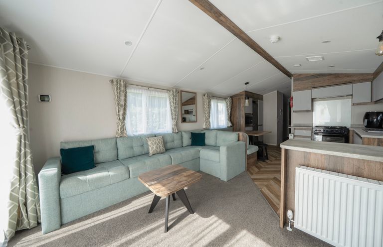A living room with a large sectional sofa and coffee table next to an open kitchen and dining area at Stillwater Retreat Billing Aquadrome Holiday Park