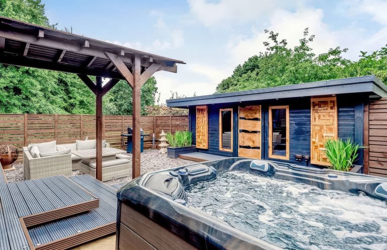 An outdoor patio with a hot tub wooden pergola seating area and a dark wooden cabin at Orchard Retreat Staycation in Kirton