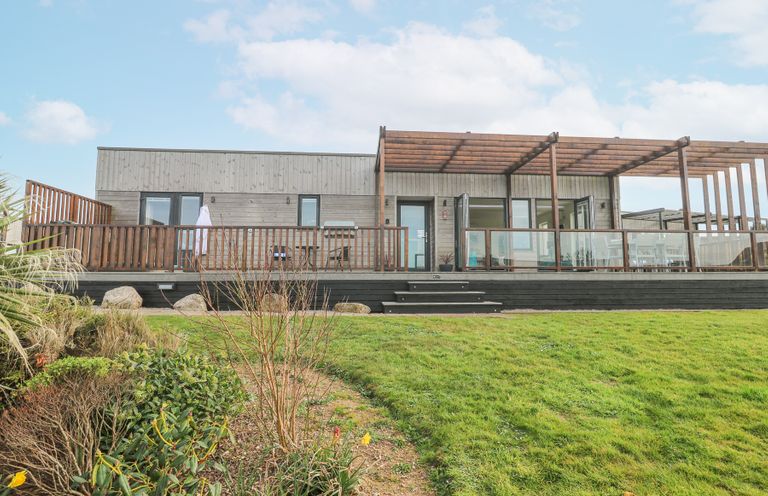 A single story wooden building with a large deck and pergola overlooking a garden at Hepworth in Portreath