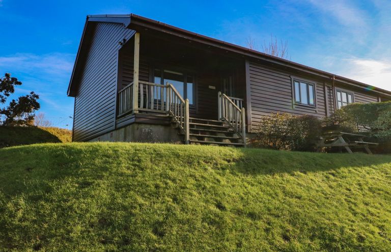 A wooden cabin with a small staircase and railing on a grassy hill at Glen Mhor Lodge in Arisaig