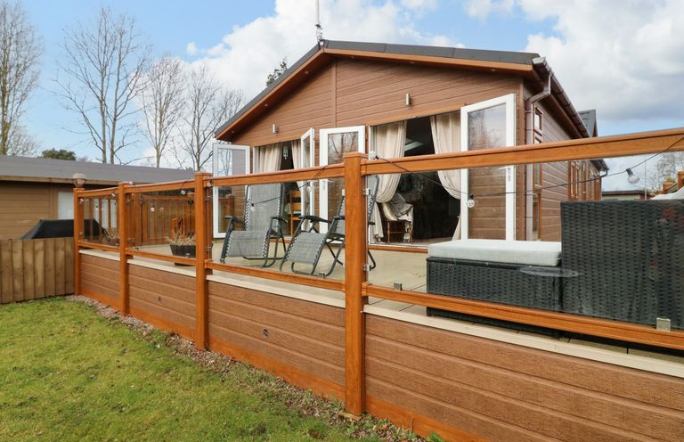 An outdoor patio with chairs and a sofa enclosed by a glass and wood railing at The Lake House in Marston near Barkston