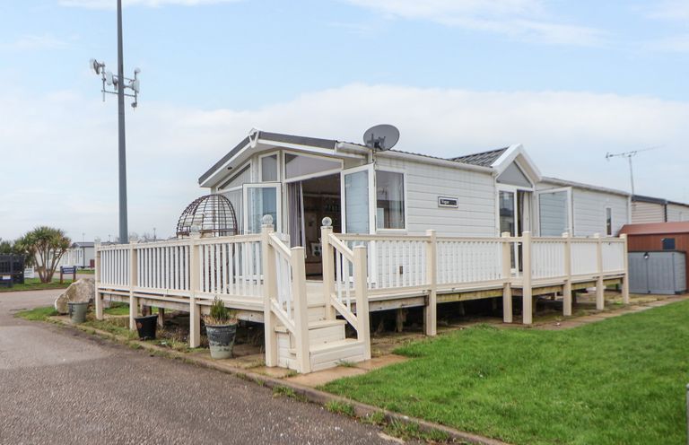 A mobile home with a fenced wooden deck and steps in a residential area at Hazel Park Lodge HP4 in Rhyl