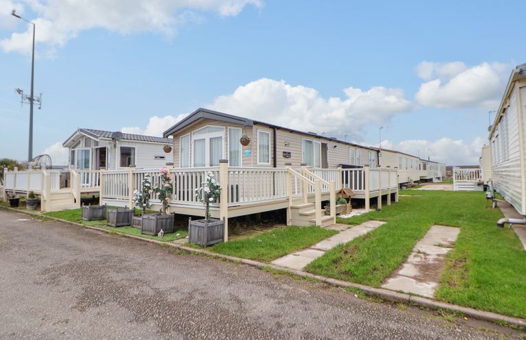 A row of beige mobile homes with white railings and steps on a grassy area at Hazel Park 11 HP11 in Rhyl
