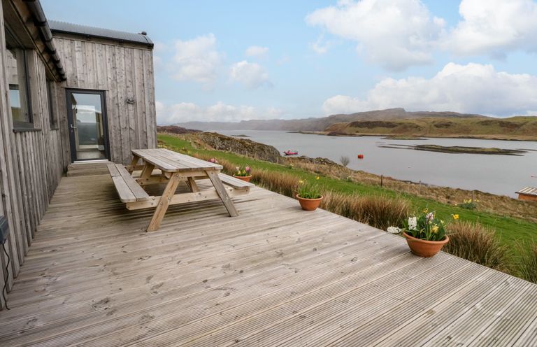 An outdoor wooden deck with a picnic table and potted plants overlooking a body of water at WildLuing Cullipool Isle Of Luing